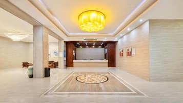 A hotel lobby with a reception desk, a chandelier, and a patterned floor.