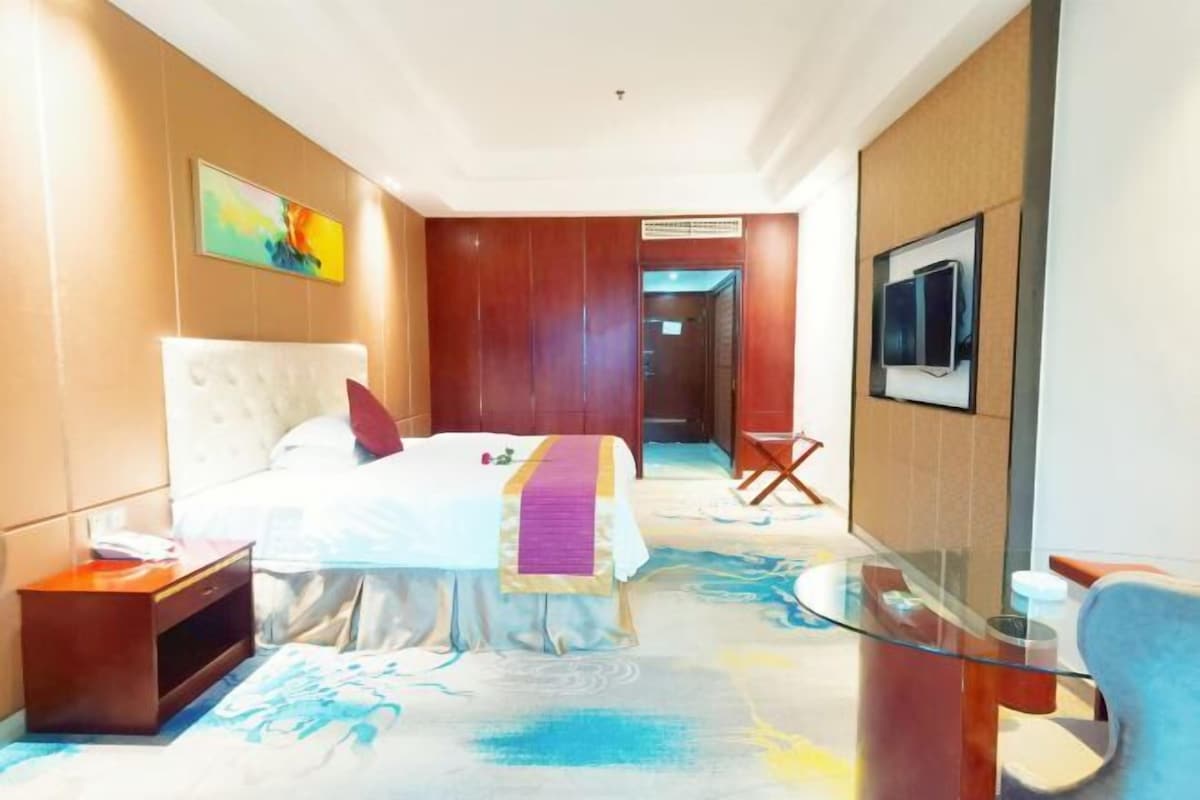 A hotel room with a bed, bedside table, and a glass partition separating the bed from the seating area.