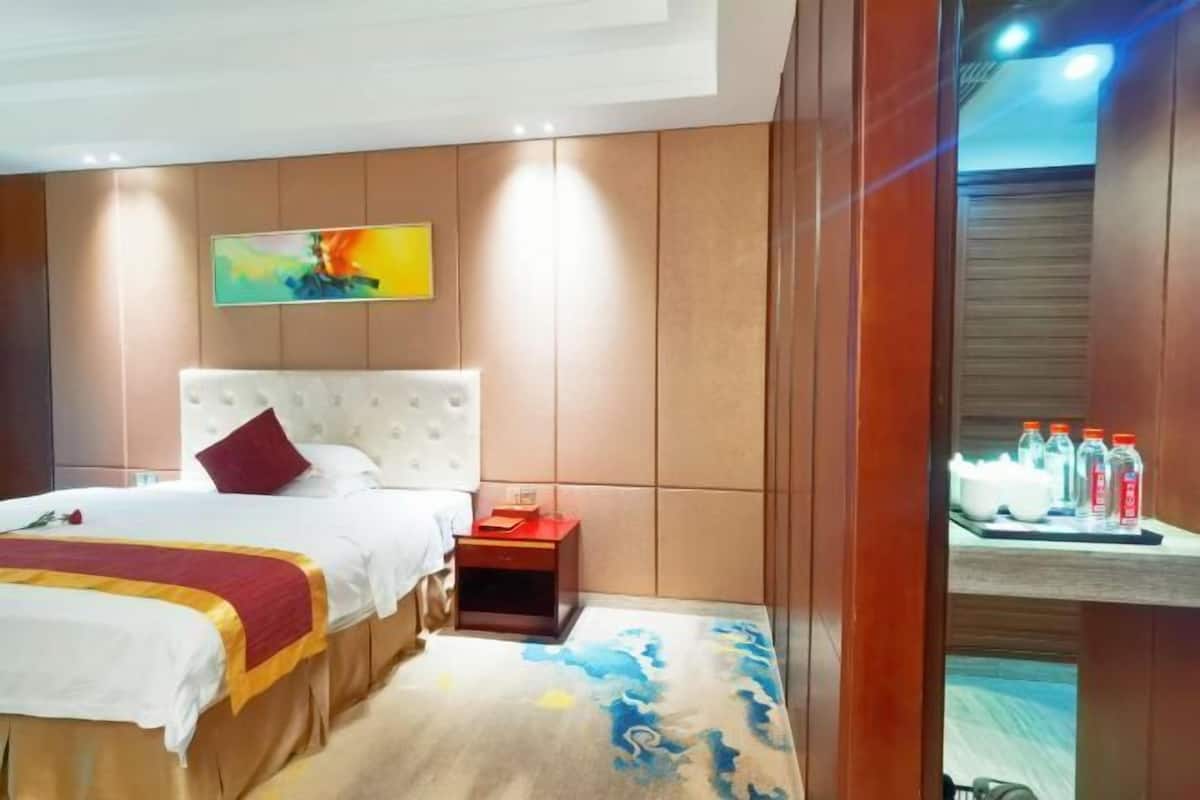 A hotel room with a bed, a nightstand, a painting on the wall, and a shelf with bottles.