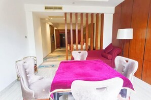 A hotel room with a dining area featuring a table with a pink tablecloth, white chairs, and a wooden partition. - Ruixia Business Hotel (Renhua)