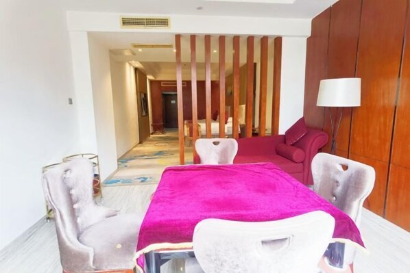 A hotel room with a dining area featuring a table with a pink tablecloth, white chairs, and a wooden partition. - Ruixia Business Hotel (Renhua)
