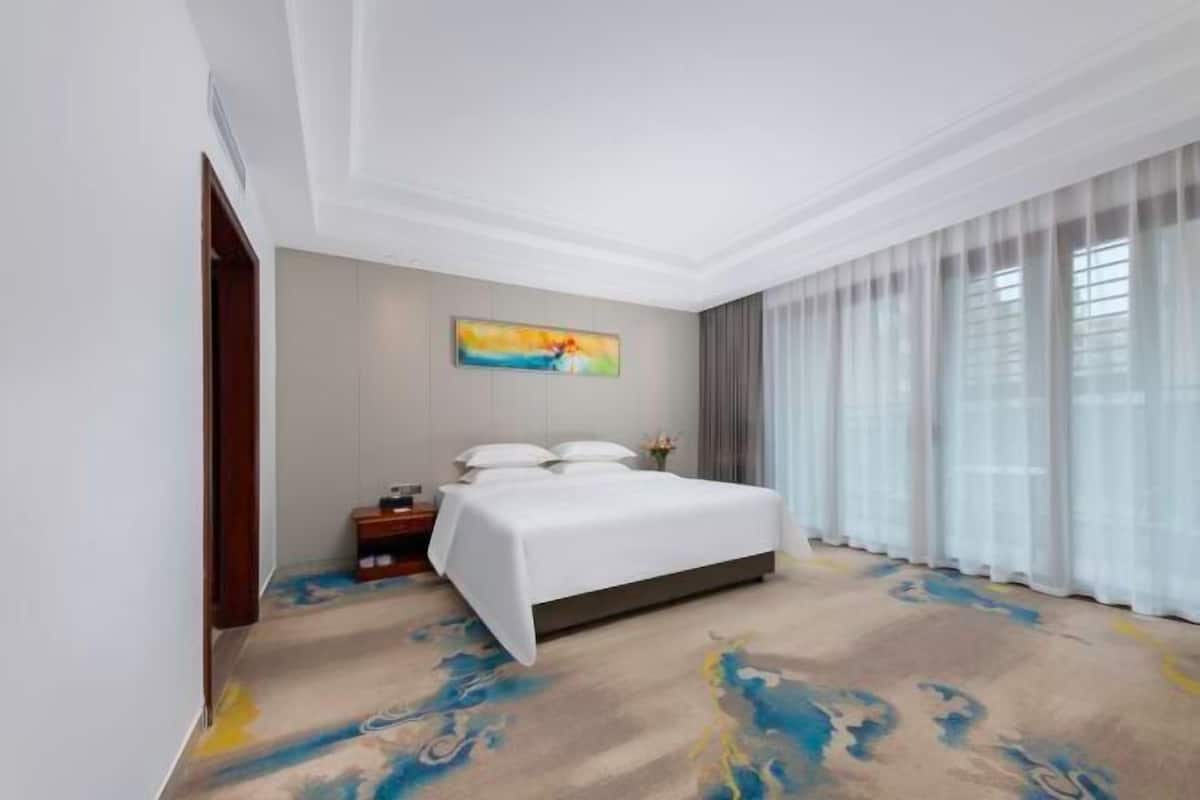 A hotel room with a large bed, a nightstand, a painting on the wall, and a window with curtains.