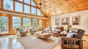Amplia sala de estar con ventanas grandes, techo de madera y vistas al exterior.