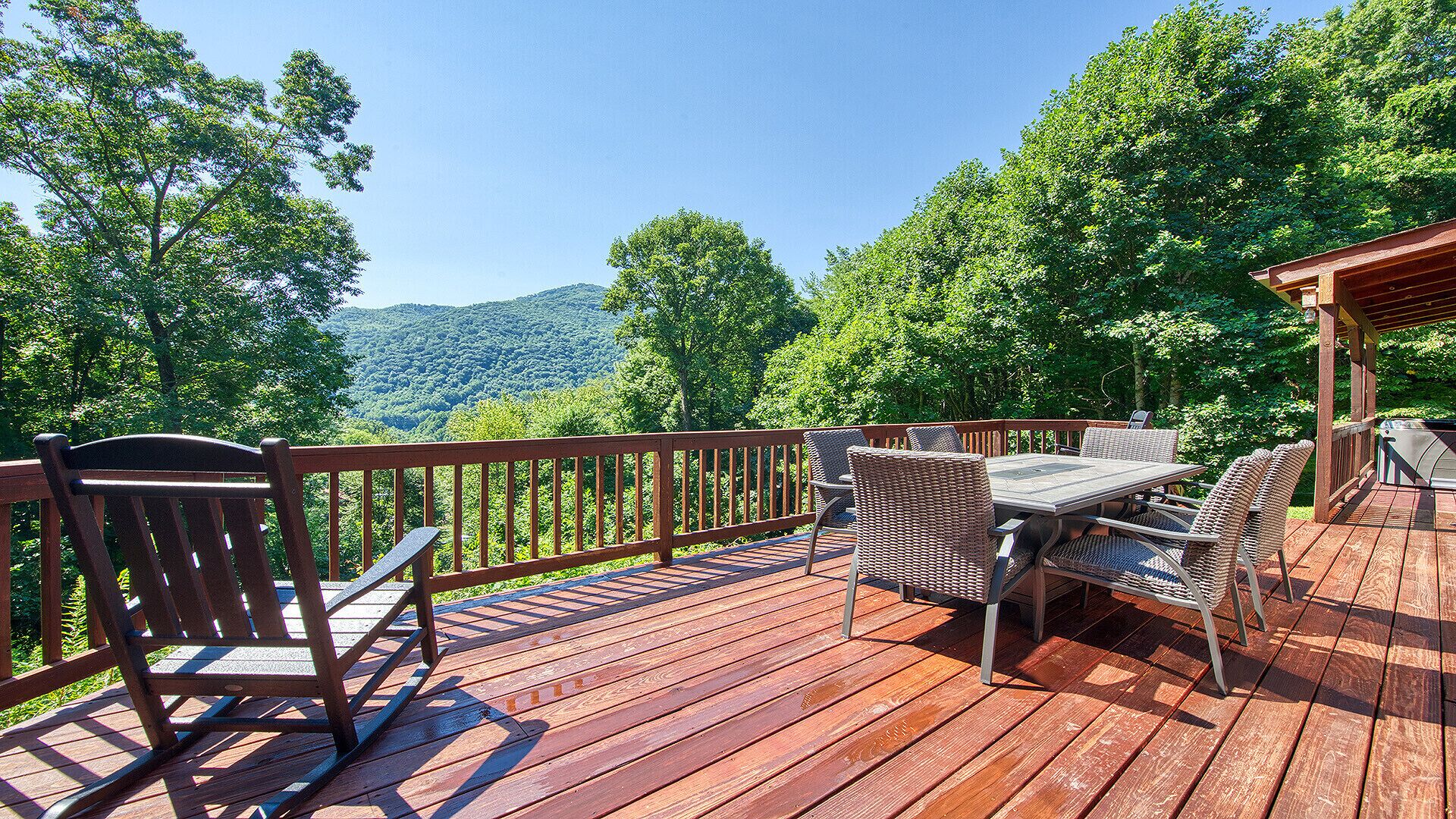 Une terrasse en bois, agréée de mobilier d’extérieur, notamment des chaises et une table, qui offre une vue sur une zone boisée avec une montagne en arrière-plan.