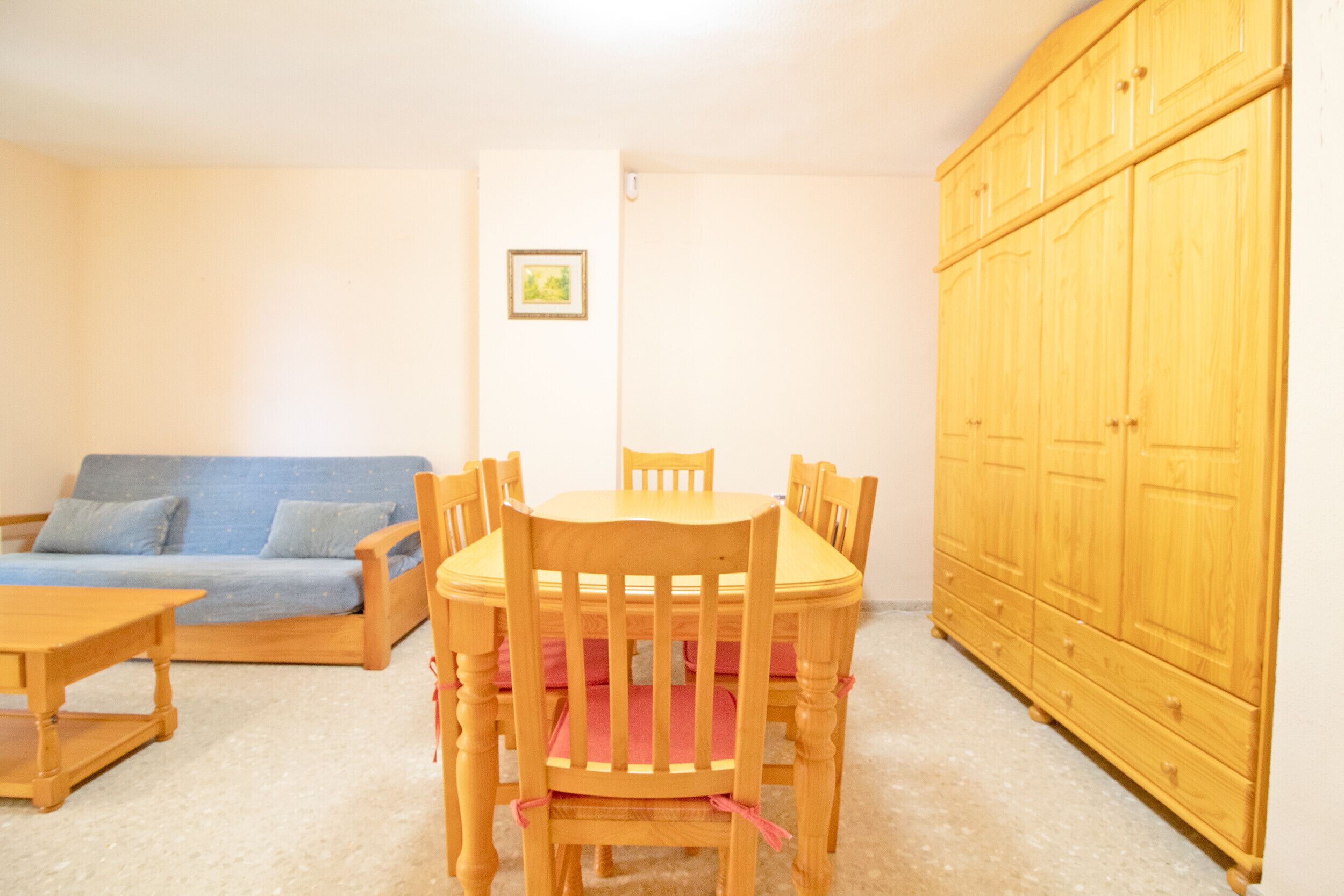 Een kamer met een houten eettafel, omringd door stoelen, een blauwe bank en een houten garderobe.