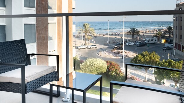 Ein Balkon mit Korbmöbeln, Blick auf den Strand und geparkte Autos.