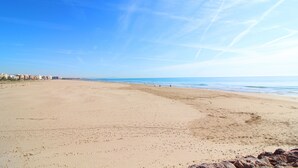Ein weiter Sandstrand mit blauem Himmel und dem Meer im Hintergrund.