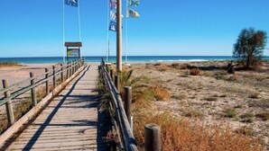 A wooden boardwalk leading to a beach with flags and a small structure. - Global Vacacional: Front line beach townhouse with sea views (Sagunto)