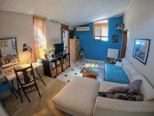 Un espace de vie compact comprenant un canapé, une petite table basse, un bureau avec une chaise et un téléviseur.