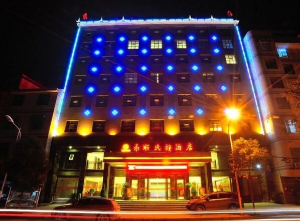 A multi-story hotel with illuminated blue lights on the facade, a red sign with Chinese characters, and a well-lit entrance. - Yongshun Minzu Hotel (Yongshun)
