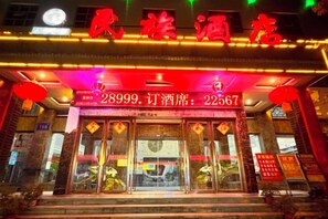 A hotel entrance with a red neon sign, a visible phone number, and a traditional Chinese architectural style.