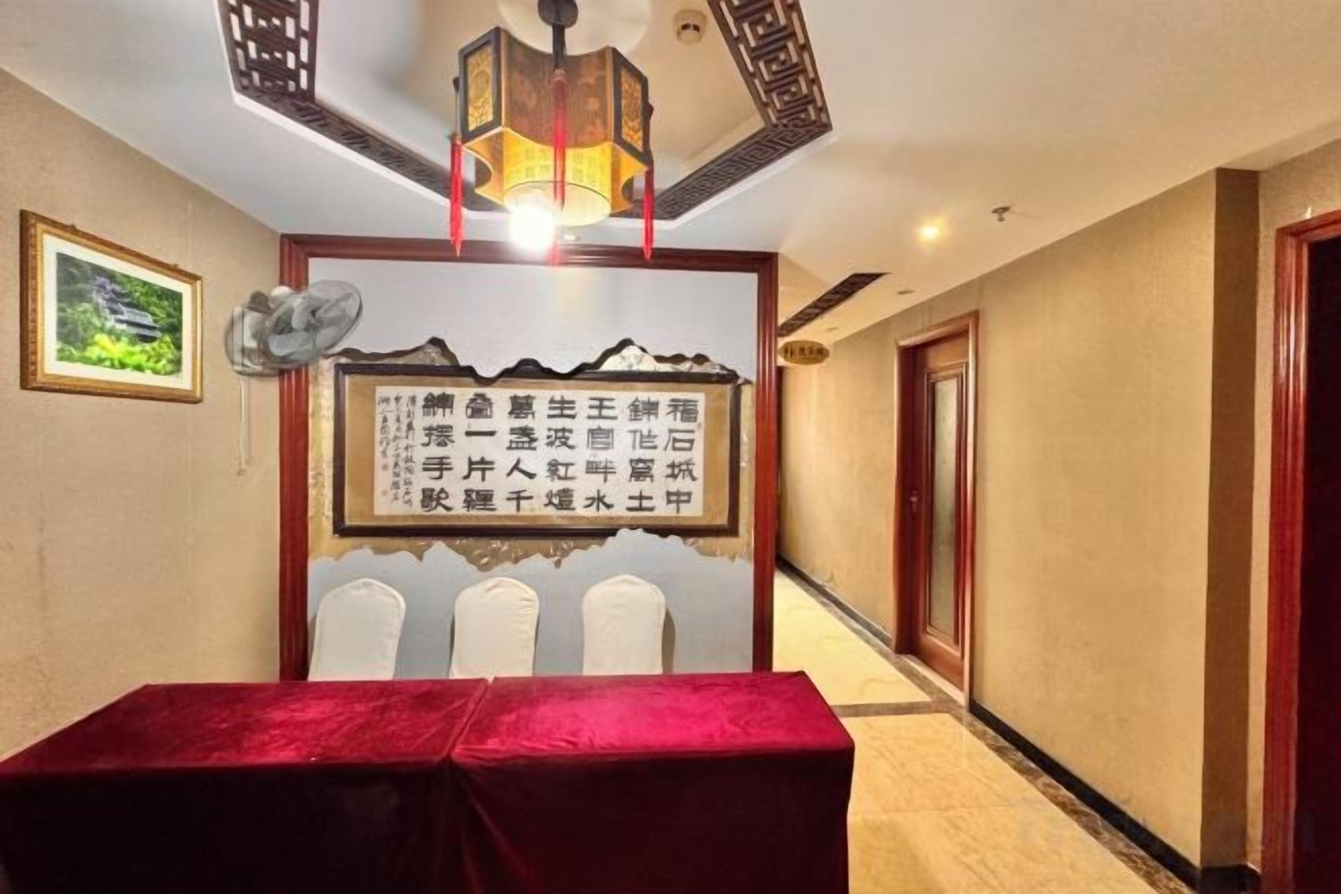 Una habitación de hotel con una mesa roja, un ventilador de pared y un panel decorativo.