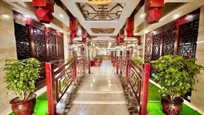 A corridor with a traditional design, featuring a central staircase, red railings, and potted plants on either side. - Yongshun Minzu Hotel (Yongshun)