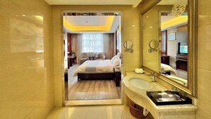 A hotel room with a bed, a bathroom with a mirror and sink, and a view of another room. - Yongshun Minzu Hotel (Yongshun)