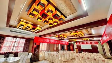 A banquet hall with rows of round tables and chairs, a decorative ceiling, and a red banner.