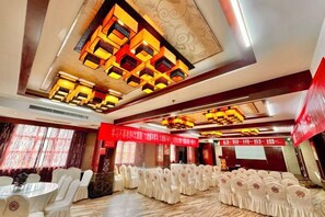 A banquet hall with rows of round tables and chairs, a decorative ceiling, and a red banner.