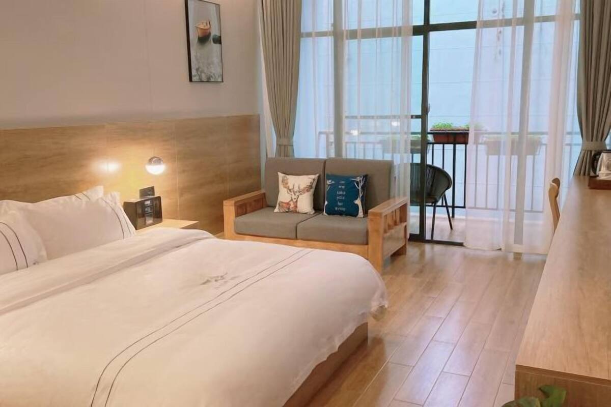 Habitación de hotel con una cama grande, un sofá, una mesita y un balcón con vistas.