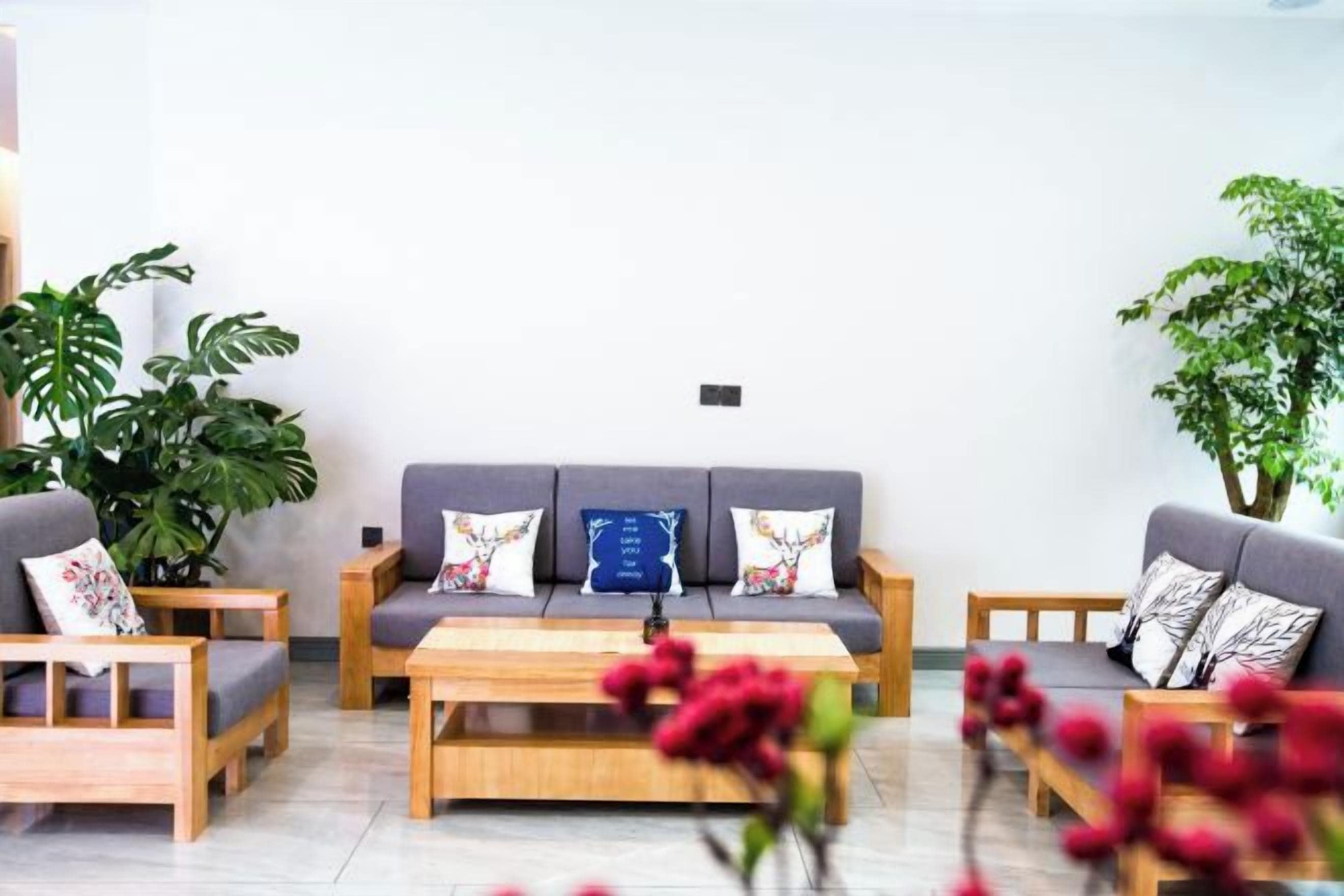 Ein modernes Wohnzimmer mit einer Sofagarnitur, einem Couchtisch und zwei Beistelltischen. Übertöpfe mit Pflanzen und eine Vase mit Blumen sind ebenfalls vorhanden.