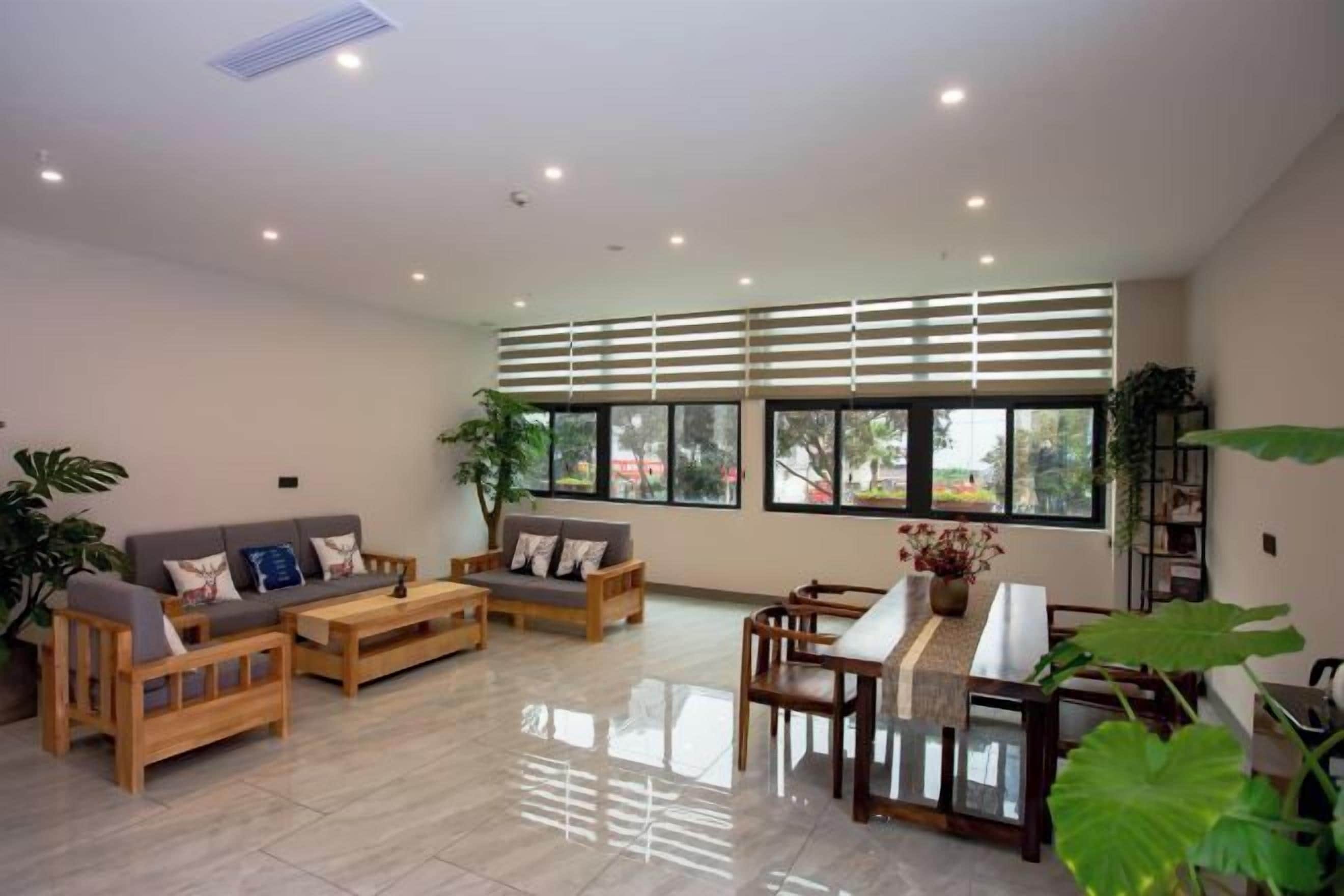 A spacious living room with a sofa set, a dining table, and large windows with blinds.