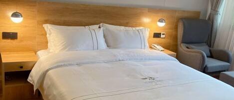 A hotel room with a wooden headboard, a bed with white bedding, a bedside table with a lamp, and a chair.