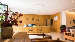 Un espace d’accueil d’hôtel comprenant un comptoir de réception en bois, deux chaises, une plante en pot et une table en bois.