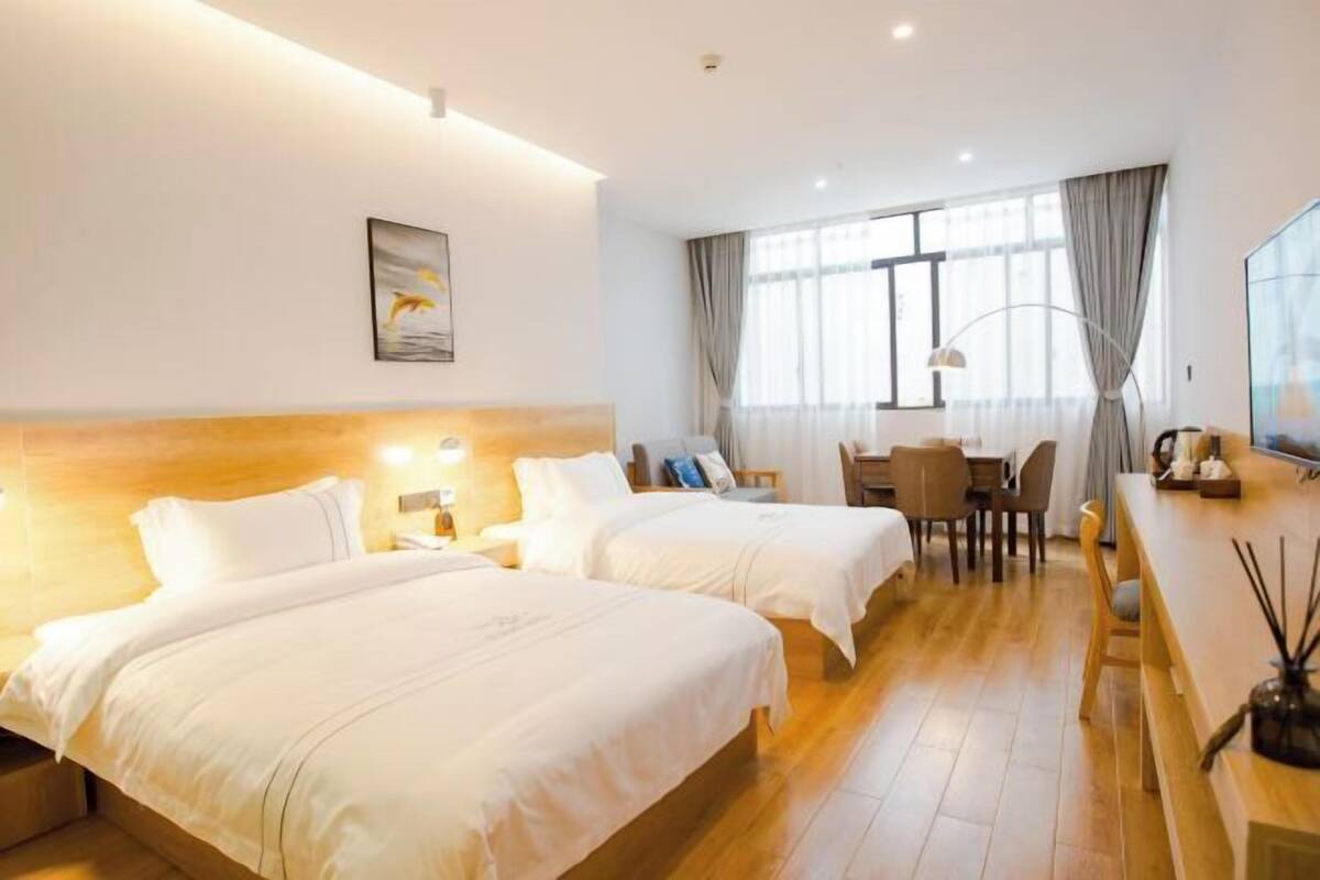 Habitación de hotel con dos camas, un escritorio, una silla, una lámpara y un cuadro en la pared.