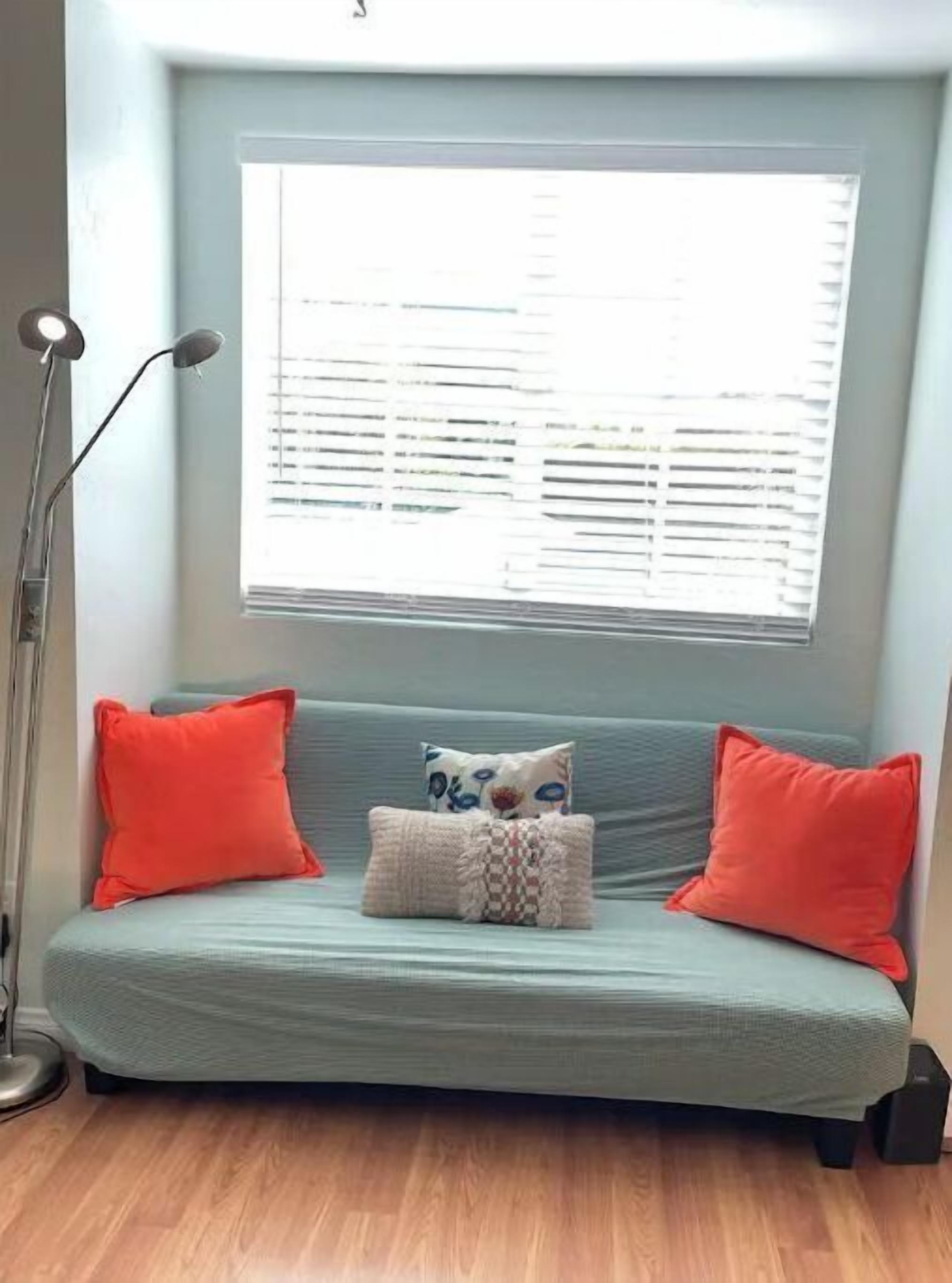 Una habitación con un sofá azul claro, dos almohadas rojas, un cojín estampado y una lámpara de pie.