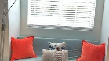 Una habitación con un sofá azul claro, dos almohadas rojas, un cojín estampado y una lámpara de pie.
