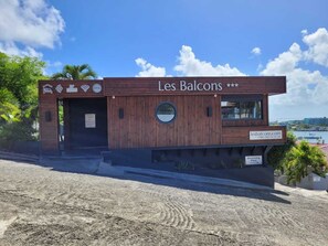 A modern building named 'Les Balcons' with a wooden facade, a swimming pool sign, and a website address.