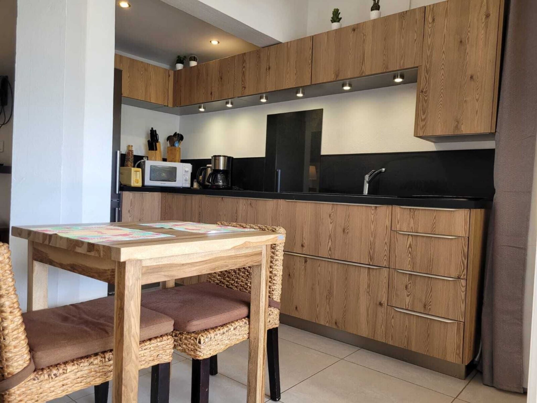 A modern kitchen with wooden cabinets, a black countertop, and a dining area with a table and chairs.