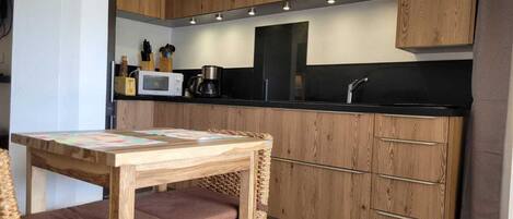 A modern kitchen with wooden cabinets, a black countertop, and a dining area with a table and chairs.