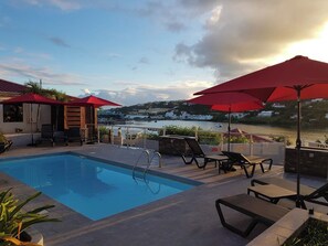 A swimming pool with lounge chairs and umbrellas, overlooking a body of water with buildings in the background.