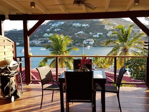 A covered outdoor seating area with a view of a body of water and hills.