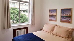 A bedroom with a bed, a window with curtains, and two framed pictures on the wall.