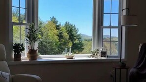 A room with a large window, a potted plant, a small table with decorative items, and a lamp. - Pine Ridge Manor • A+ Privacy • Pool • BBQ • Games (Franklin)