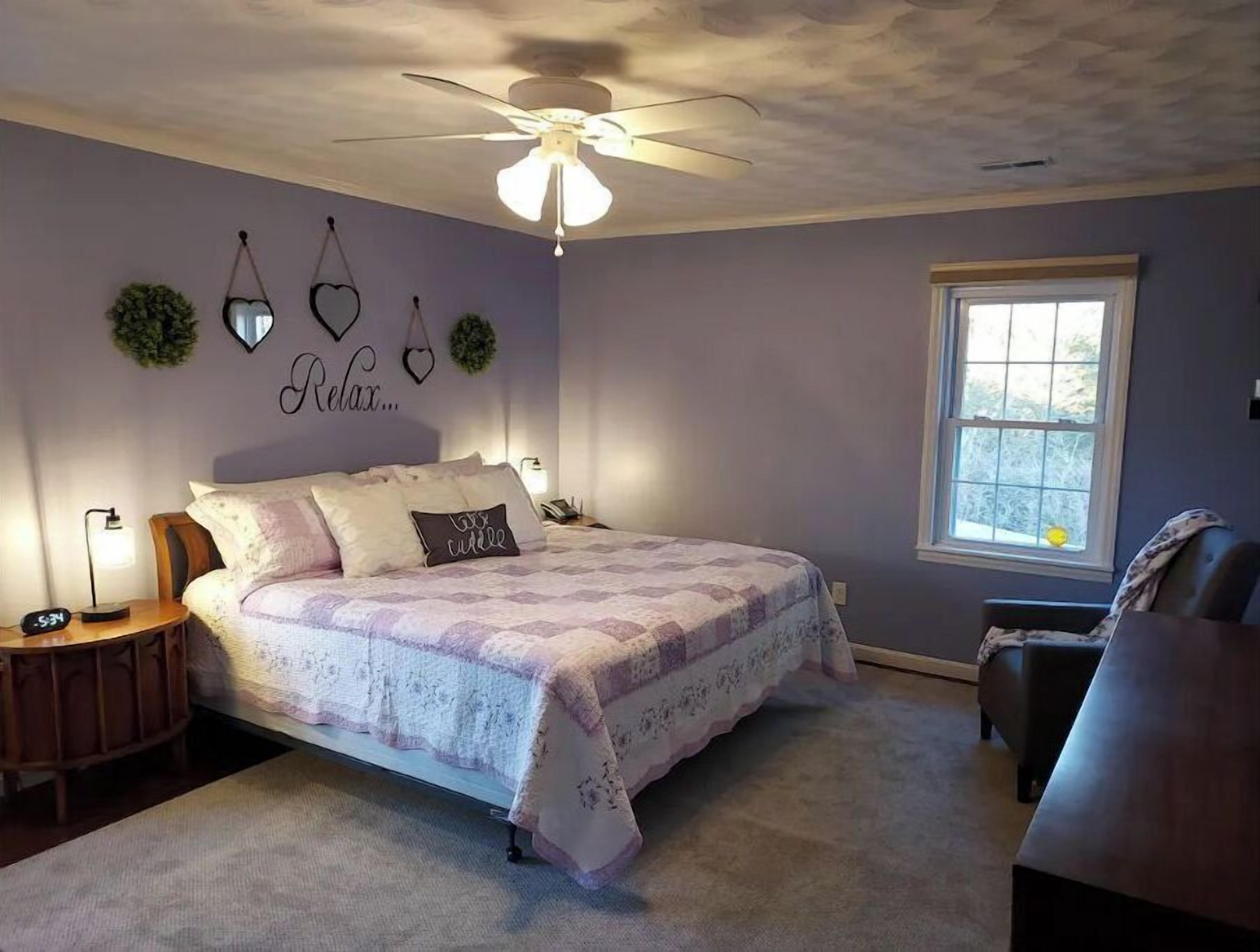 A bedroom with a bed, a nightstand, a chair, a ceiling fan, and a window.