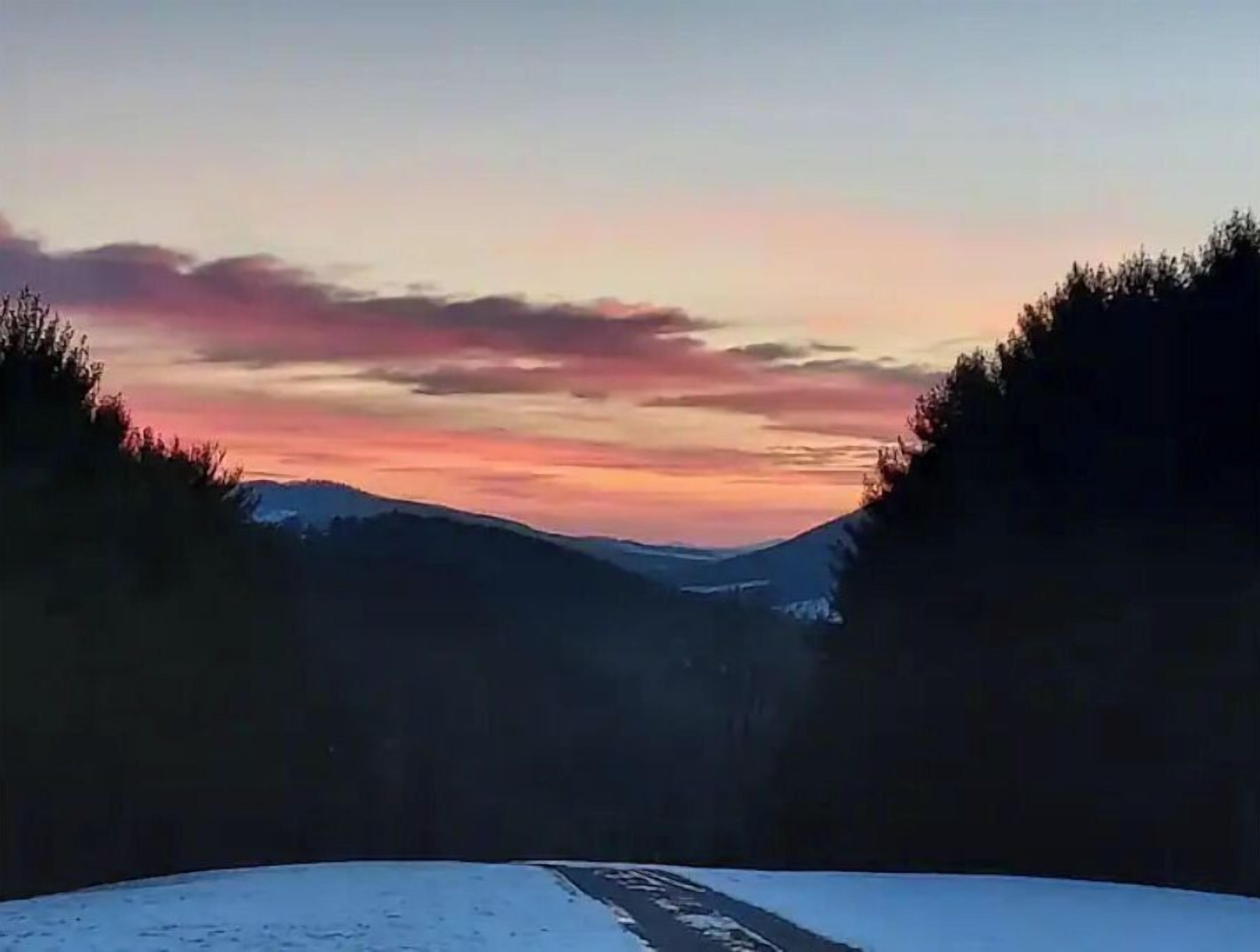 Un paysage enneigé avec une route qui traverse une vallée boisée au coucher du soleil.
