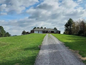 A house with a gravel driveway leading to a garage, surrounded by green grass and trees. - Pine Ridge Manor • A+ Privacy • Pool • BBQ • Games (Franklin)