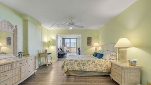 Quarto com cama, cômoda e ventilador de teto. Há um corredor que leva a outro espaço.