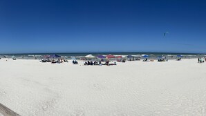 Uma extensa praia de areia com guarda-sóis e pessoas.