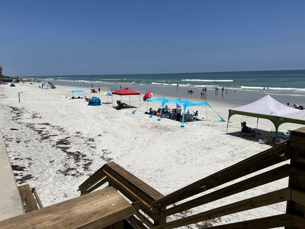 Una playa con tiendas de campaña y sillas, una terraza de madera y el océano al fondo.