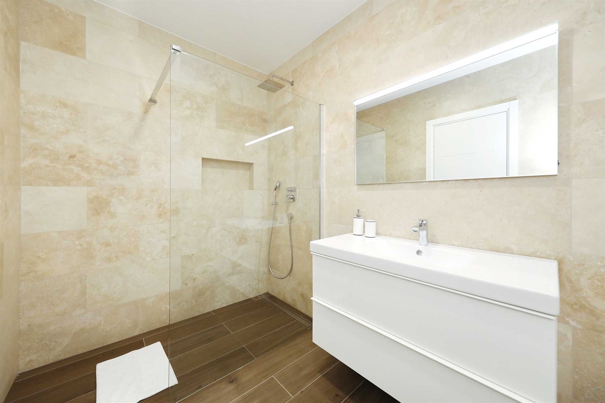 Une salle de bain moderne avec une douche à l’italienne en verre, un grand miroir et un meuble-lavabo blanc.