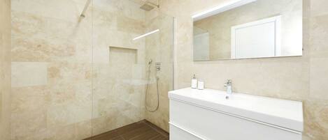 Une salle de bain moderne avec une douche à l’italienne en verre, un grand miroir et un meuble-lavabo blanc.