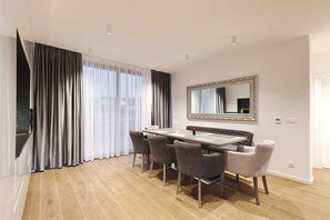 Un comedor con una mesa de madera y seis sillas, un espejo grande en la pared y vistas a través de cortinas traslúcidas.