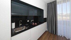 Una cocina moderna con encimera negra, pileta de acero inoxidable y una ventana con cortinas grises.