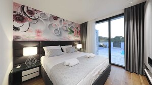 A modern hotel room with a large bed, a nightstand, a wall-mounted lamp, and a view of the outdoors through a large window. - Villa Bluebell - perfect getaway with a private pool, only 100m from the beach by MyWaycation (Pašman)