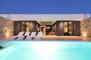 Un espace piscine extérieur moderne, doté de chaises longues et d’une table à manger.