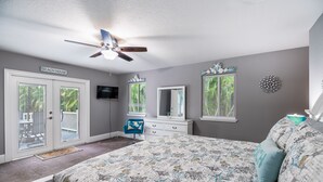 A bedroom with a bed, a ceiling fan, a dresser, a mirror, and a TV.