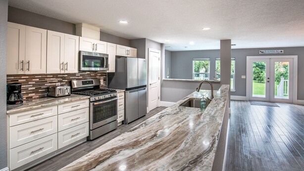 A modern kitchen with white cabinets, stainless steel appliances, and a marble countertop.