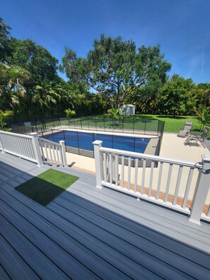 Una piscina con solárium, rodeada de una valla y árboles.